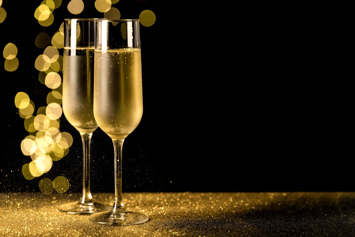 Two Champagne glasses filled with Champagne against a dark and gold backdrop